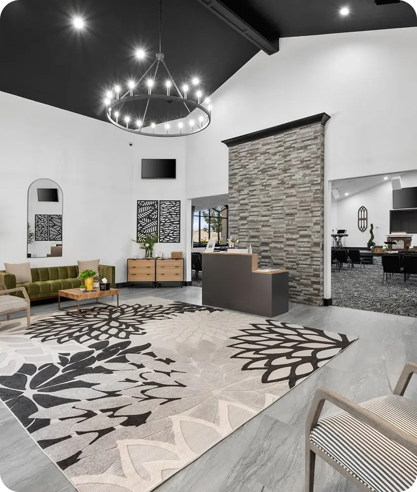 A contemporary lobby featuring a green sofa, a floral rug, and a stone feature wall under a large circular chandelier.