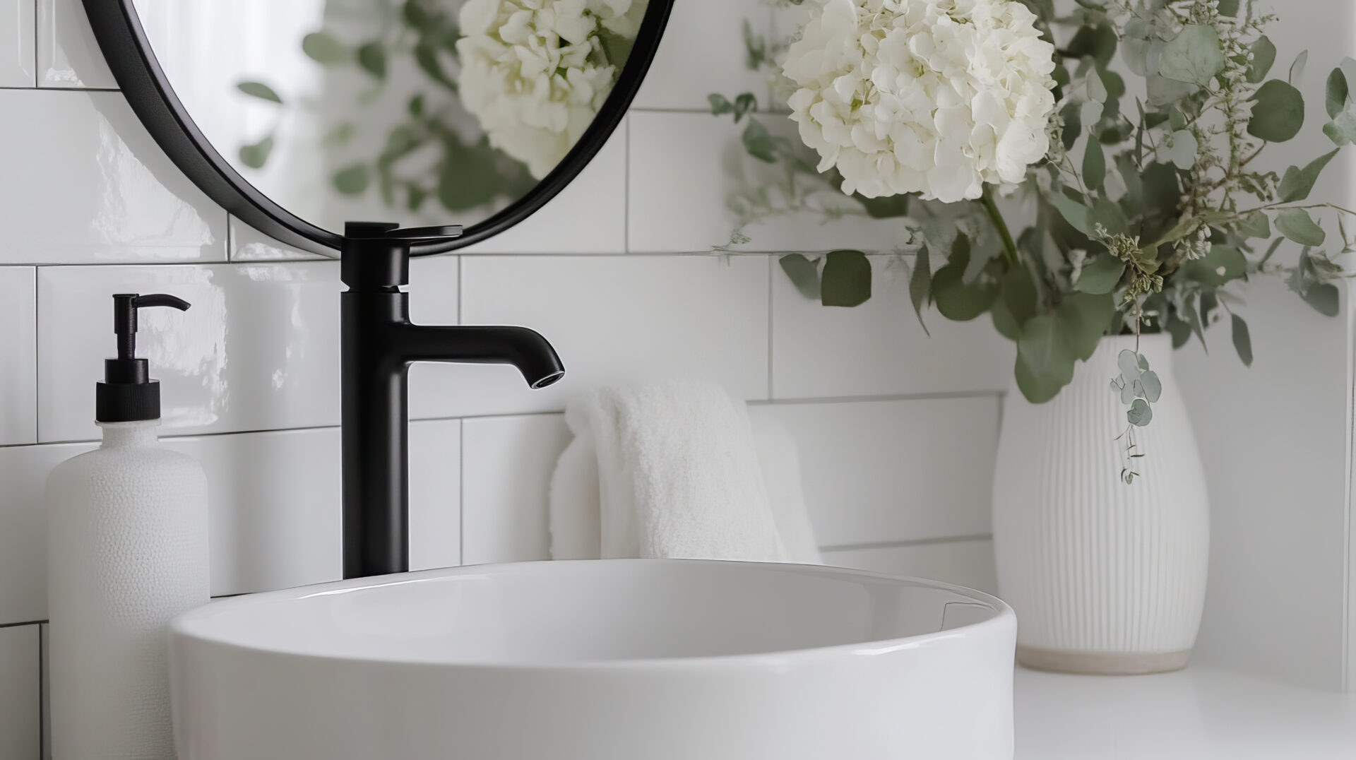 Close-up of a white bathroom vessel sink with black faucet against glossy white subway tile.